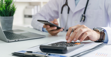 Lege ved pulten som regner på en kalkulator. Foto: Istockphoto.com/Thx4Stock