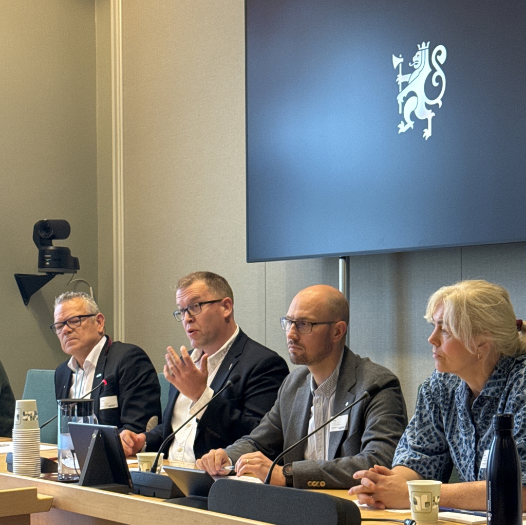 Fire mennesker sitter bak en benk med mikrofoner på.