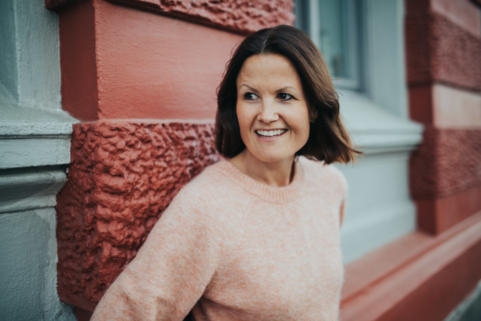 Kvinne i genser med ryggen til murvegg utenfor leilighetsbygg. Marianne Natvik foto Anita Sæle
