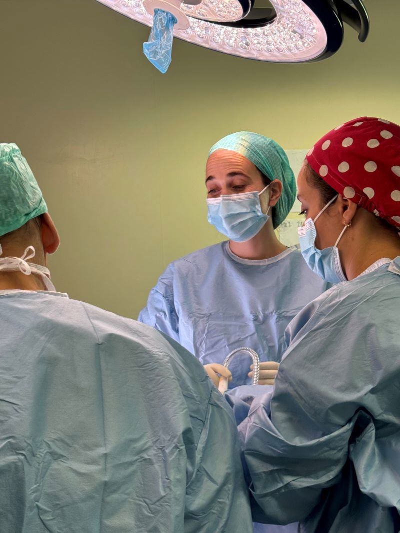 Bilde av tre kirurger som assisterer under en operasjon. To står med ryggen til kamera og den tredje er i fokus med ansiktet mot kamera. Foto: Mie Cappelen Skovholt