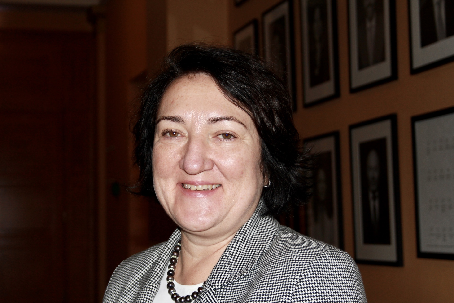 En hvit kvinne med mørkt hår, smilende, foran en bildevegg i Domus Biblioteca.