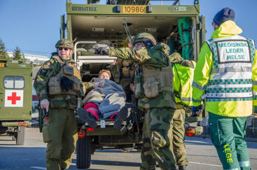 Militær ambulanse med sanitetssoldater som overleverer pasient til sivilt helsepersonell.
