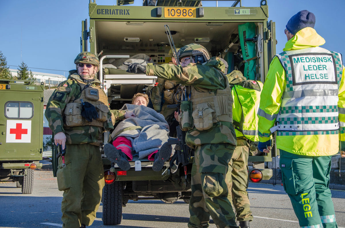 Militær ambulanse med sanitetssoldater som overleverer pasient til sivilt helsepersonell.