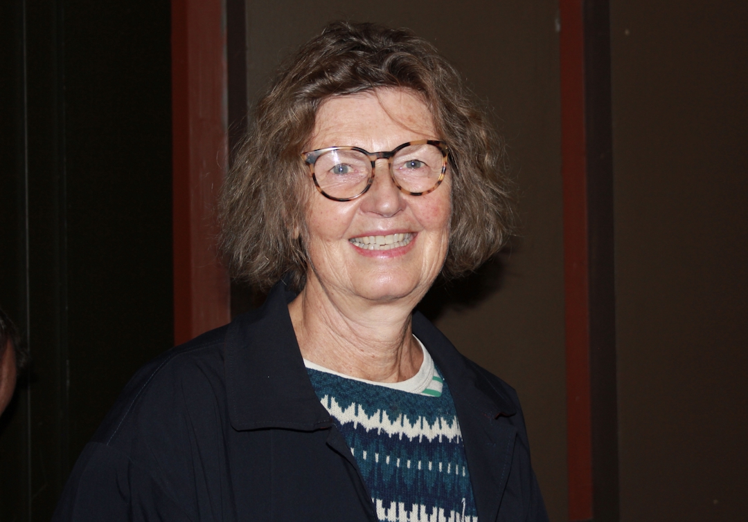 Kvinne med grått krøllete hår som smiler.