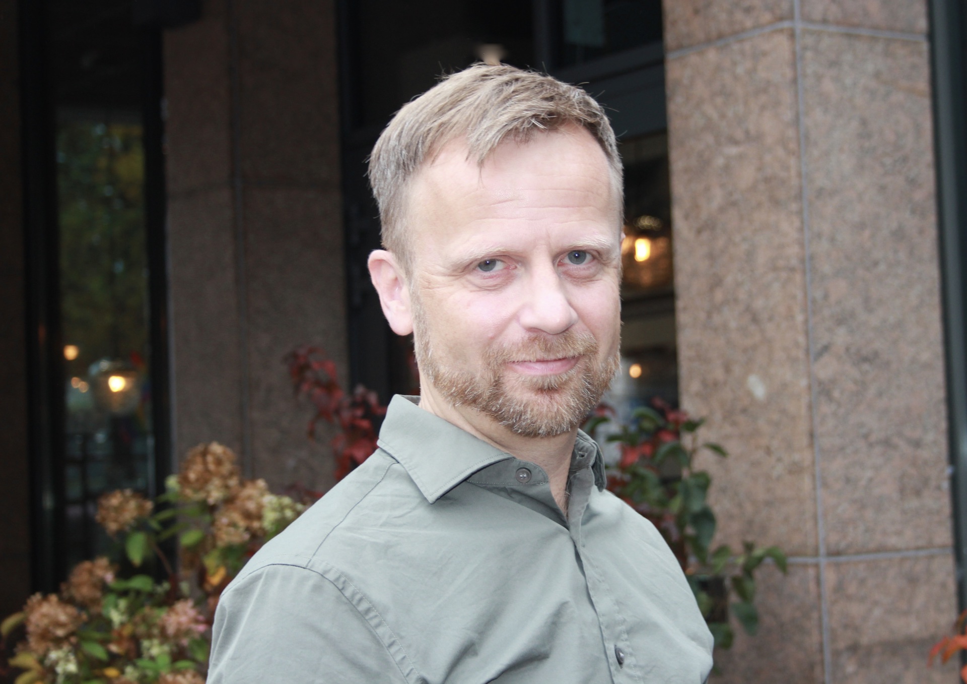 Bilde av en mann i grønn skjorte utendørs foran Legenes hus i Oslo.