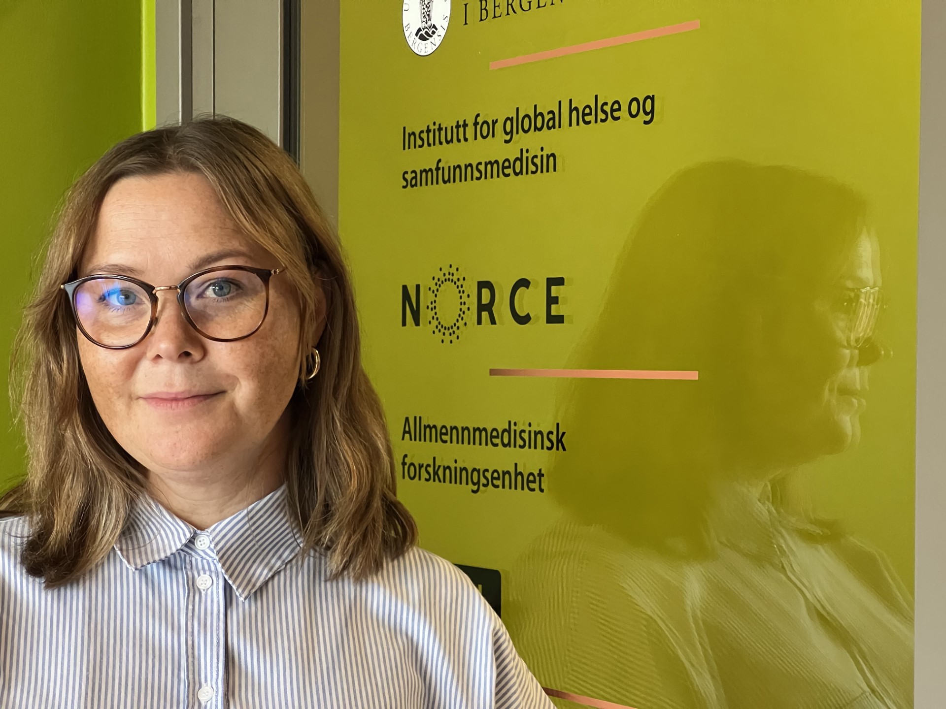 Dame med briller foran grønt skilt med navn på arbeidsplass. Heid Marie Meling. Foto: Arngeir Berge NORCE