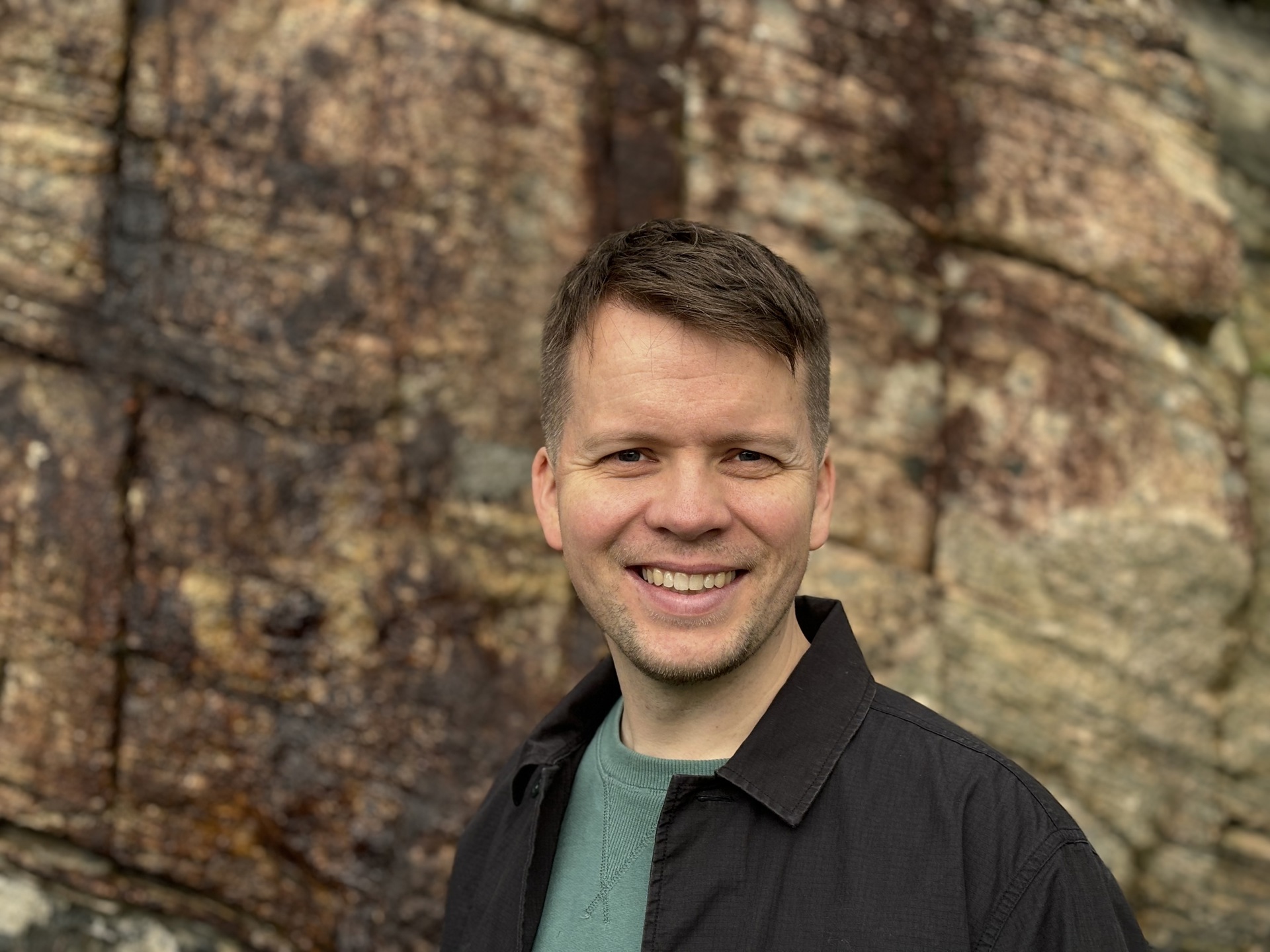 En ung mann som smiler foran en bergvegg.