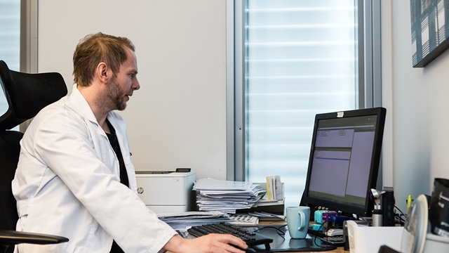 Bilde av lege som sitter foran pcen