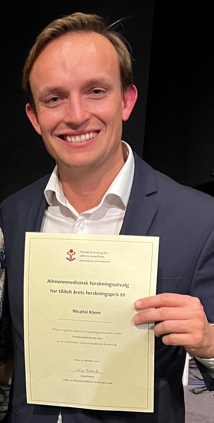 Man in suit holding diploma, Nicolay Klem award at PMU 2022. Foto Trygve Skonnord