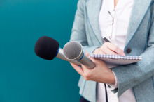 Dame som holder to mikrofoner og en notatblokk. Foto: Istockphoto.com/Mihajlo Maricic