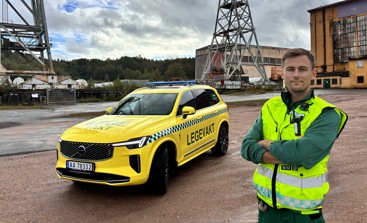 Mann i gul vest foran gul Legevakt bil