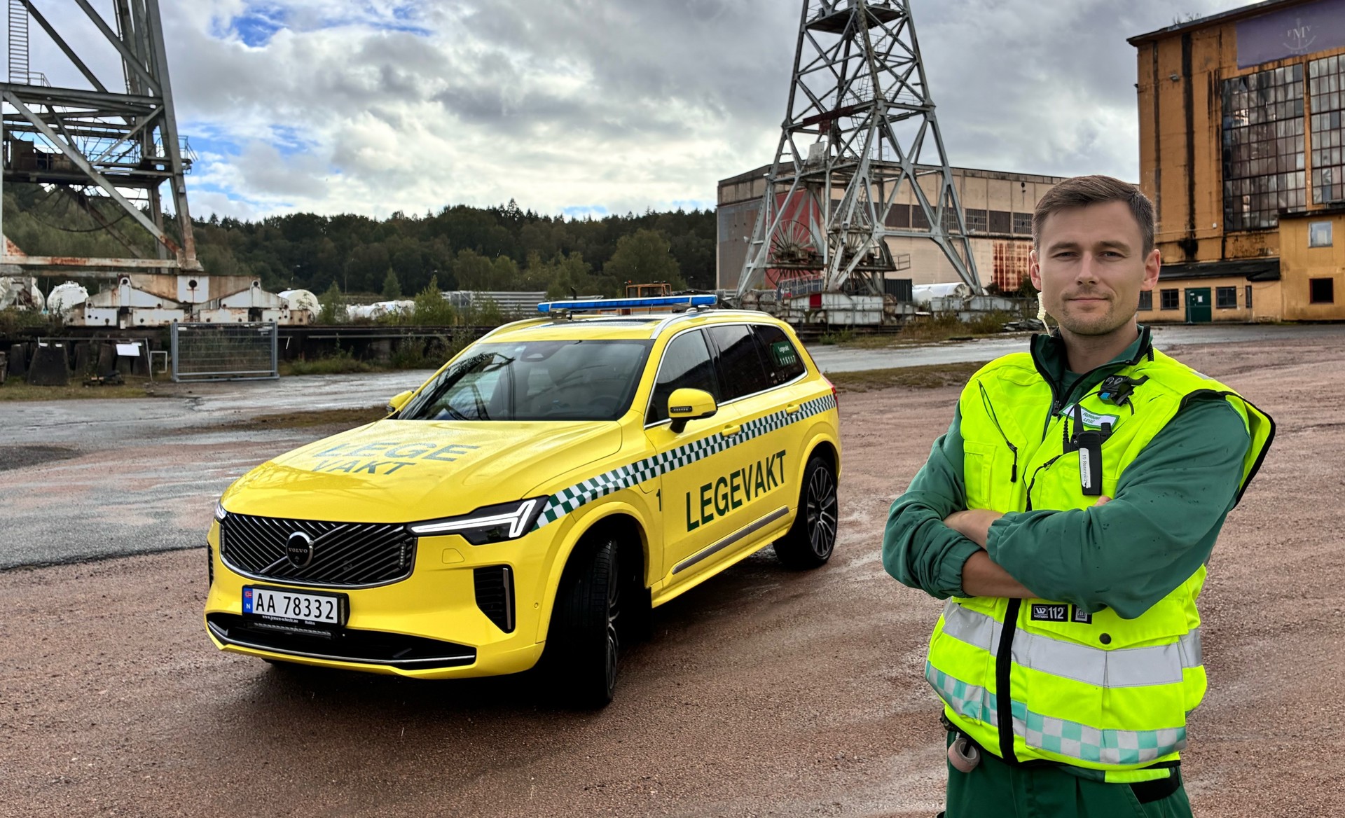 Mann i gul vest foran gul Legevakt bil