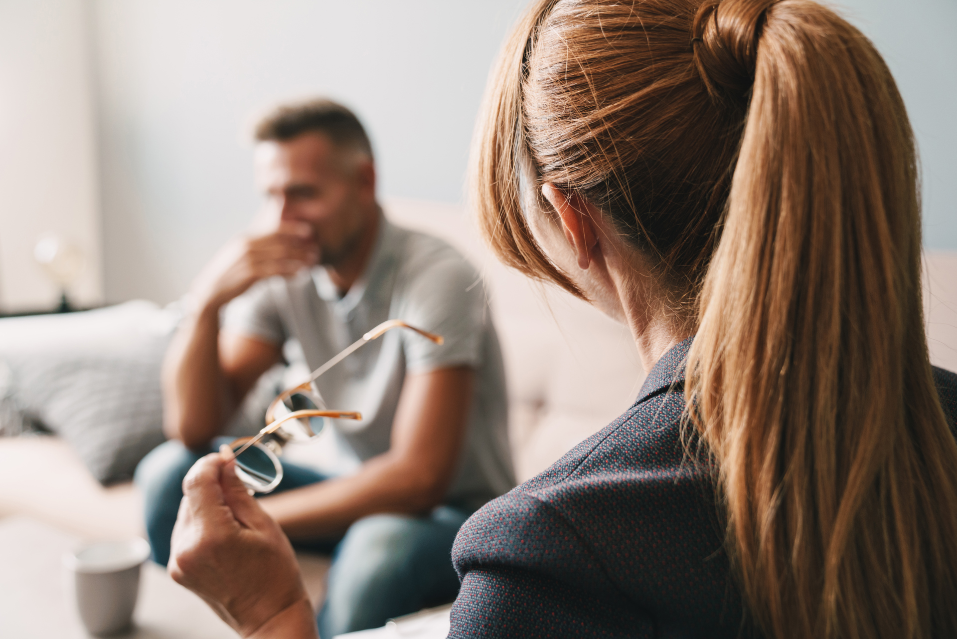 Kvinne med briller i hånden lytter til mann i sofa