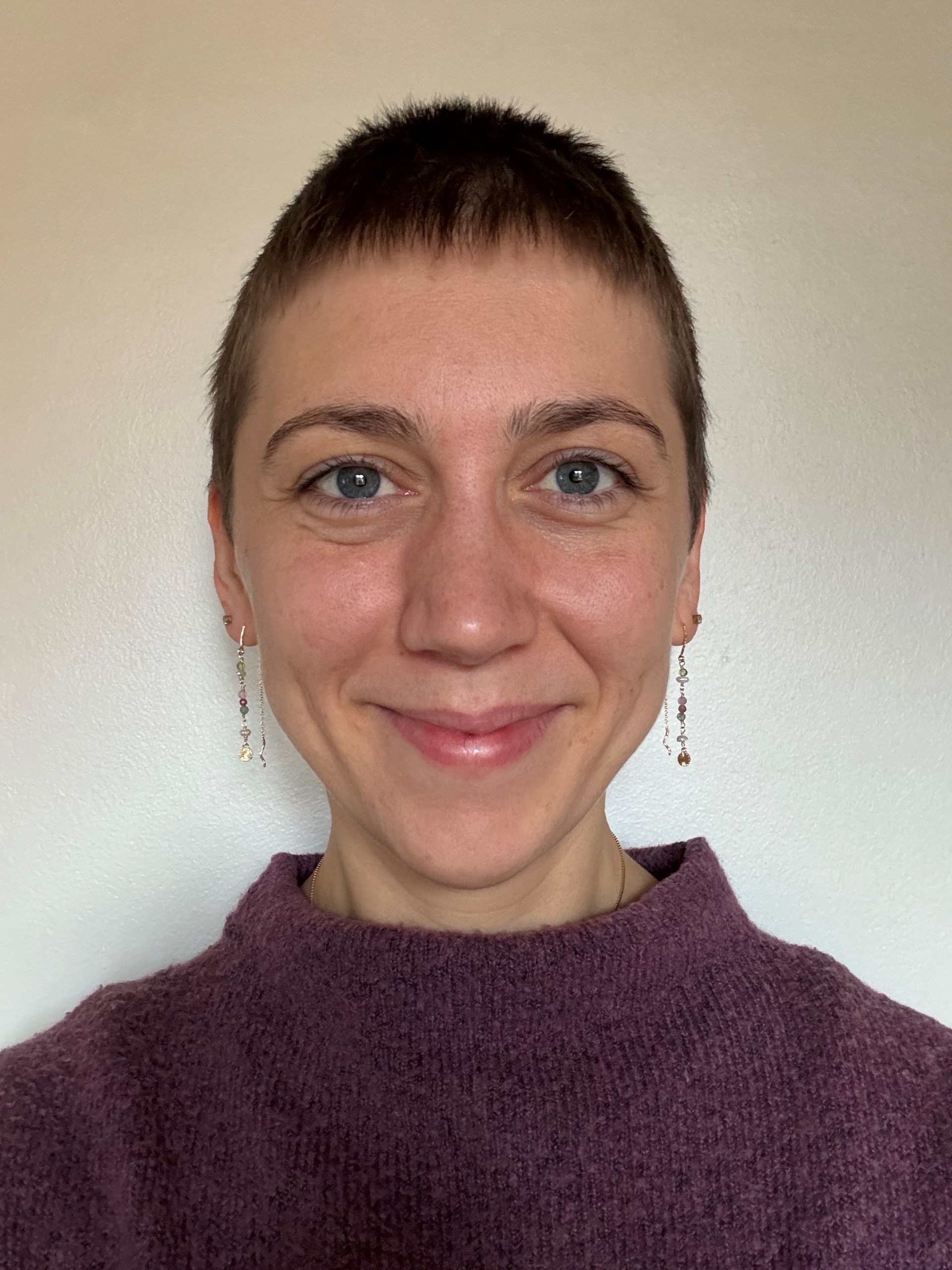 Ung kvinne i lilla genser, lang ørepynt og kortklippet hår.