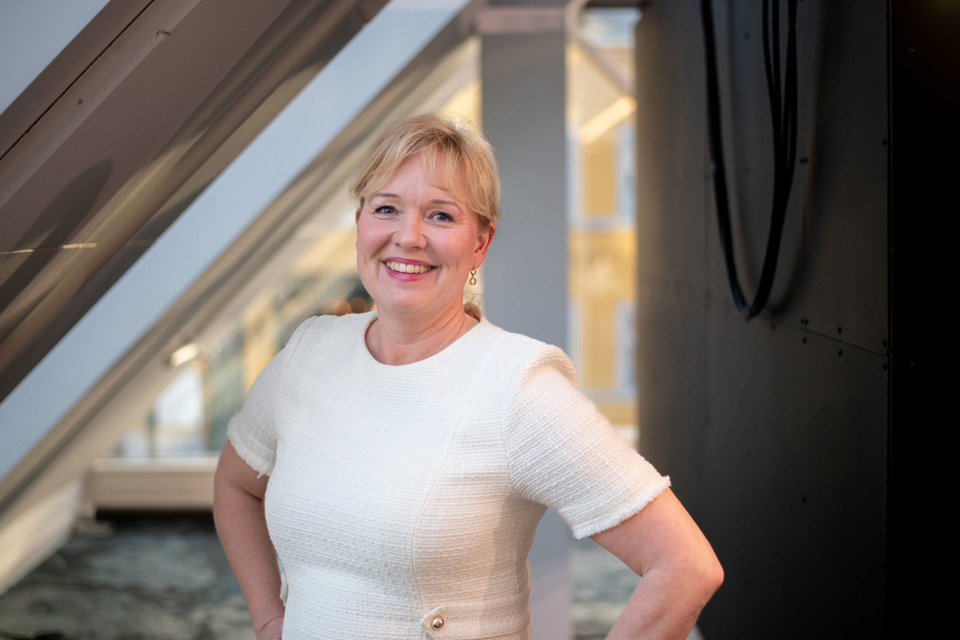 Kvinne i offwhite kjole i møterom med hendene i siden, smiler. Marte Kvittum Tangen, foto vidar sandnes