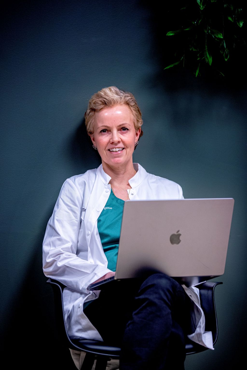 Kvinnelig lege sitter på stol inntil vegg med PC i fanget. Cathrine Abrahamsen. Foto: Peder Gjersø