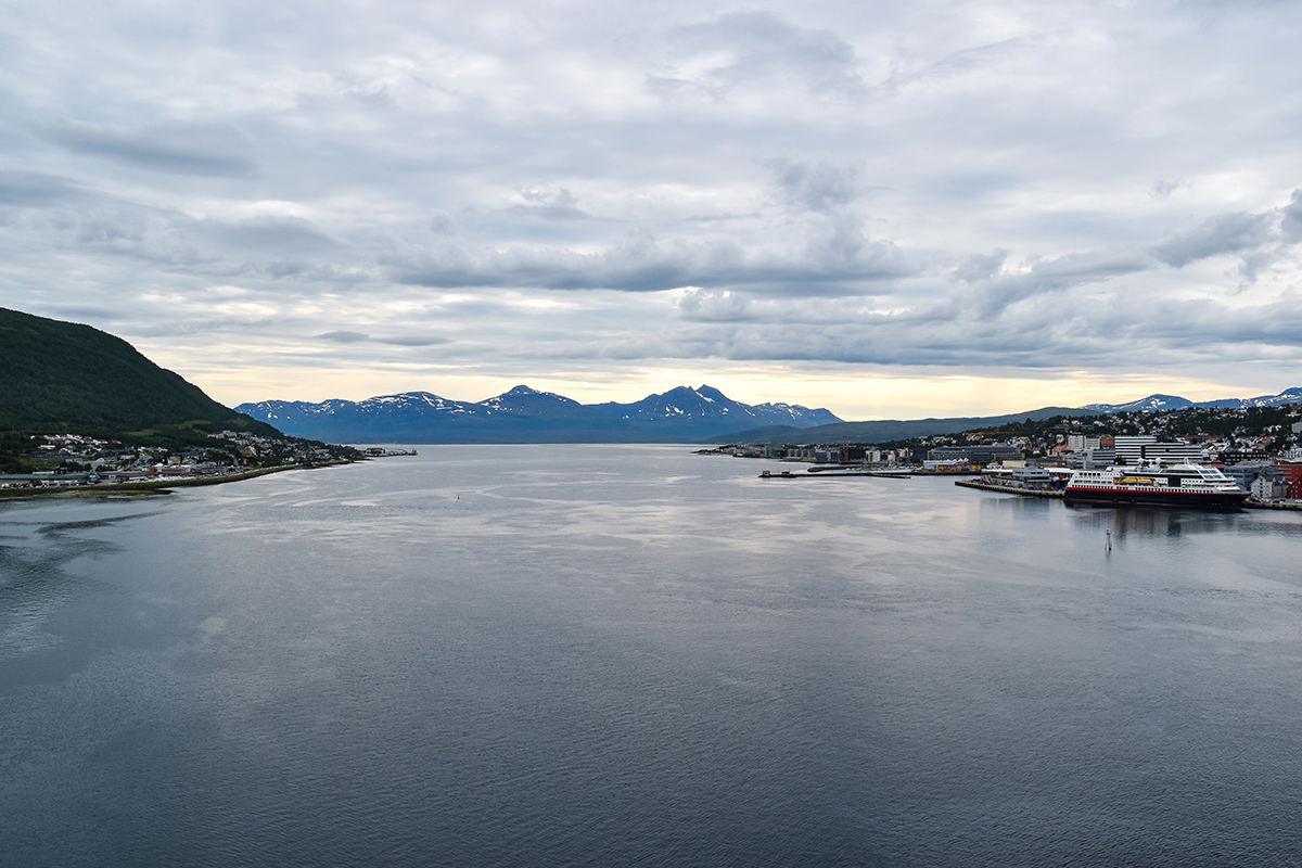 Panoramautsikt over vannkanten i Tromsø, Norge med fjellkjede i bakgrunnen under overskyet himmel.