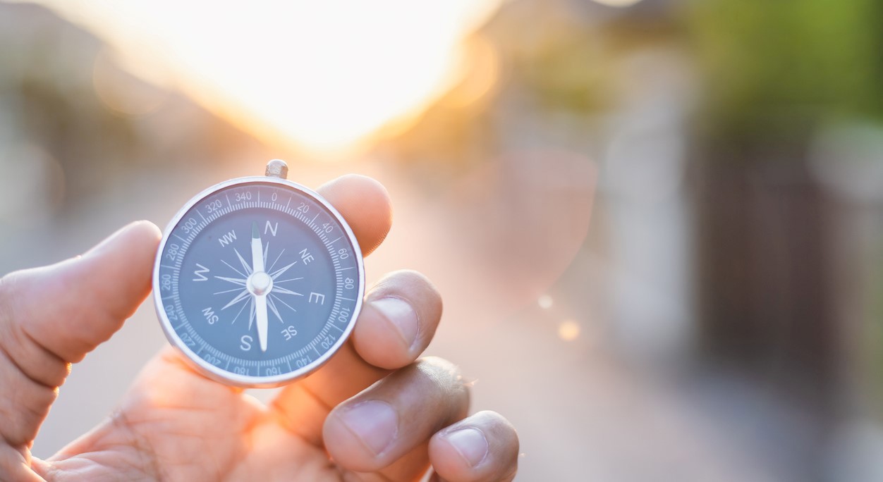 Kompass holdt i en hånd, med en utydelig solnedgang i bakgrunnen. Foto: Istockphoto.com