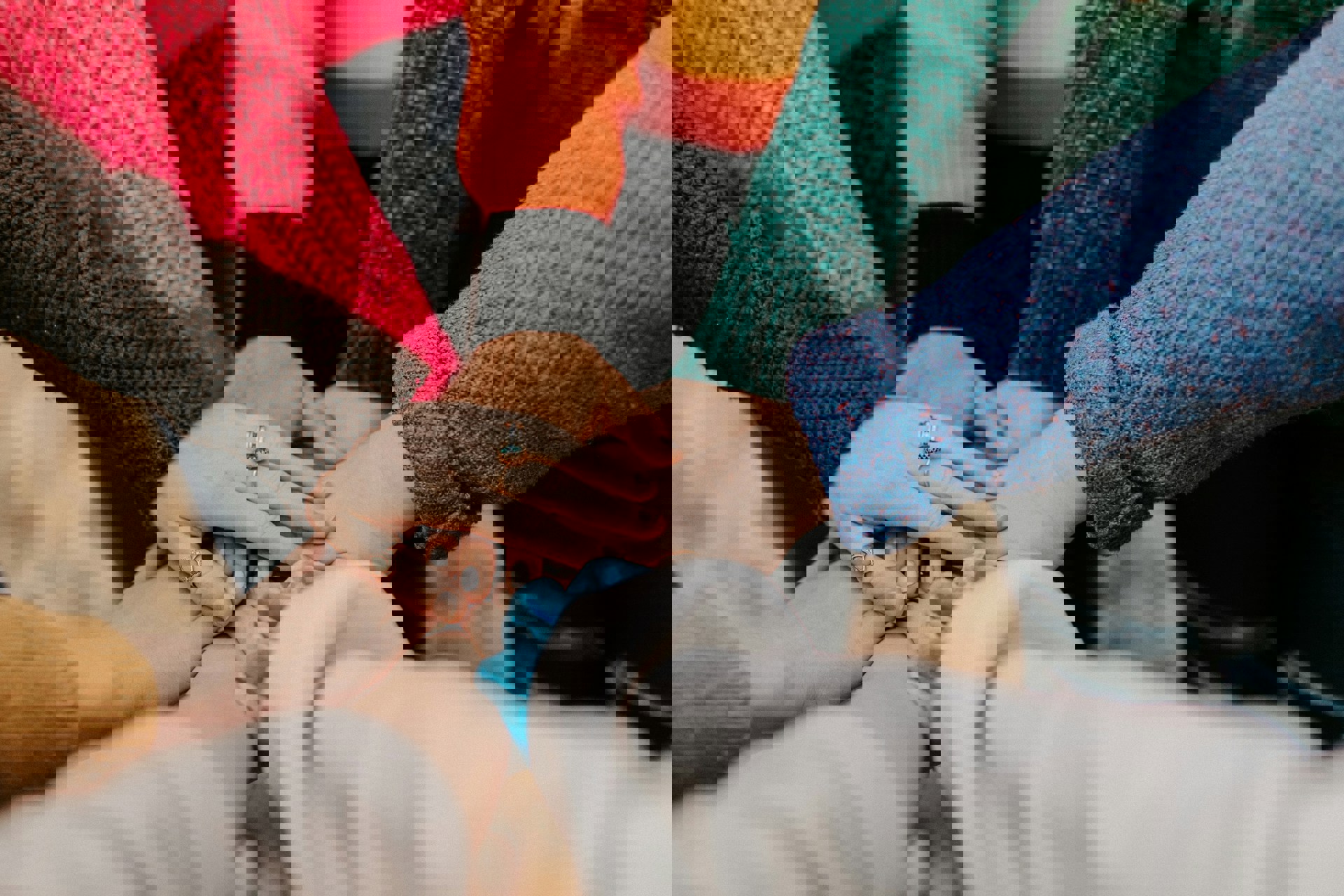 åtte armer i fargerike gensere holder hendene over hverandre i midten.