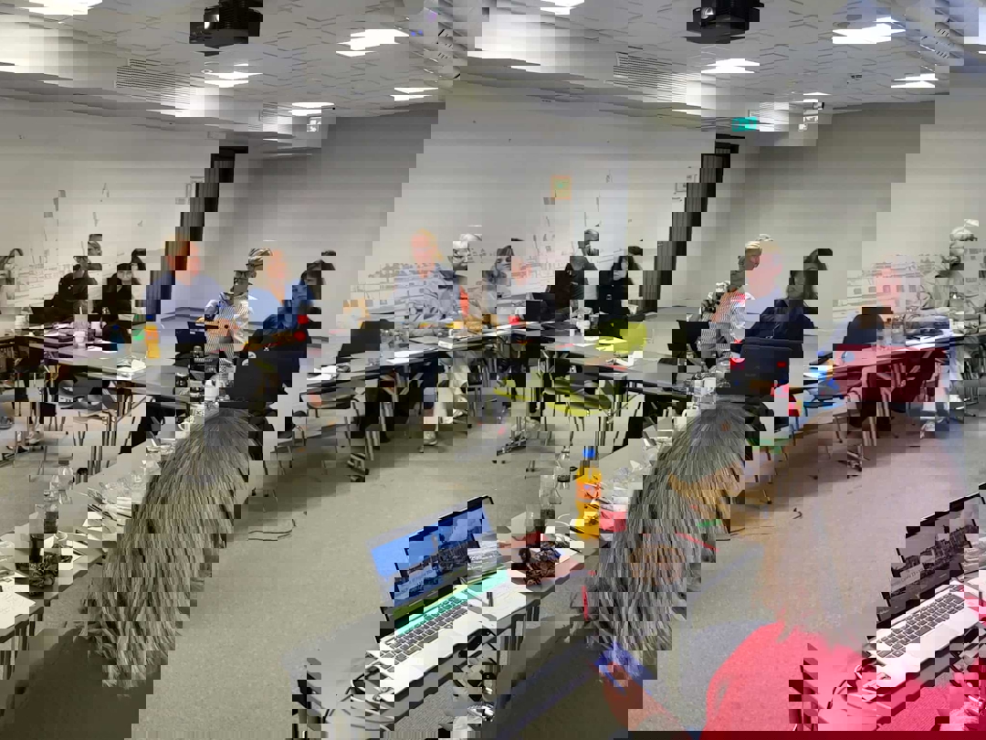 Mennesker bak bord satt i hestesko. Møterom.