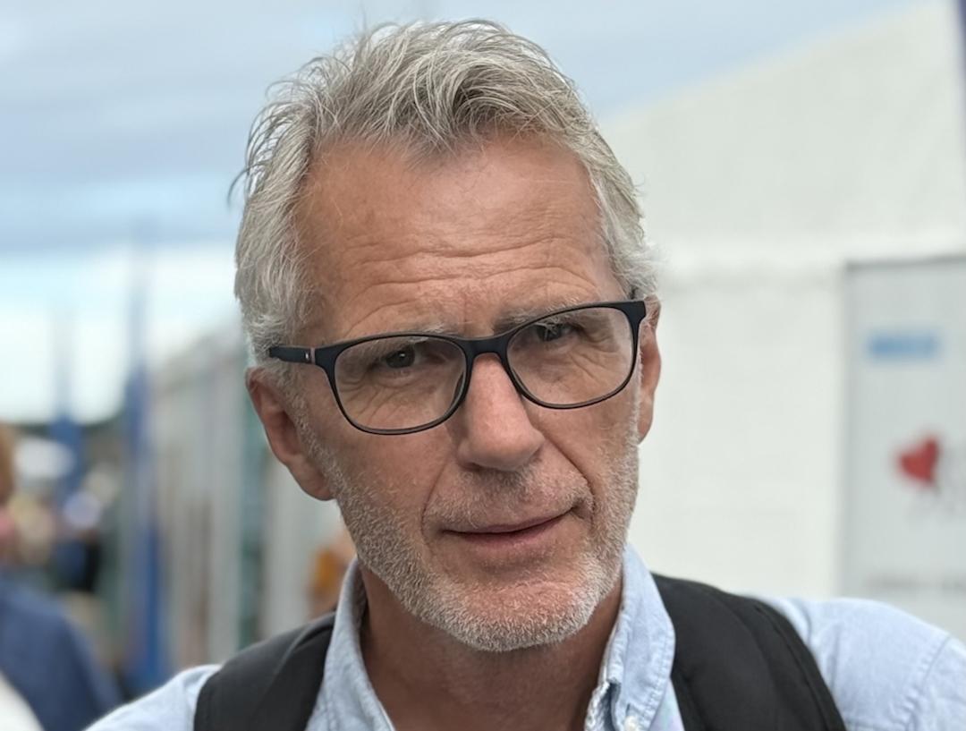 Mann med grått hår, skjegg og briller. Utendørs.