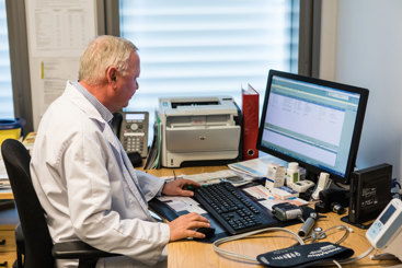 Fastlege som sitter ved en pult og jobber med en pc. Foto: Legeforneningen/Thomas B. Eckhoff