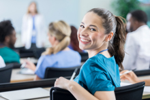 Kvinnelig medisinstudent snur seg mot kamera og smiler under en forelesning. Foto: Istockphoto.com