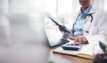 Kvinnelig lege ved en pult som trykker på en kalkulator. Foto: Istockphoto.com/Jacob Wackerhausen